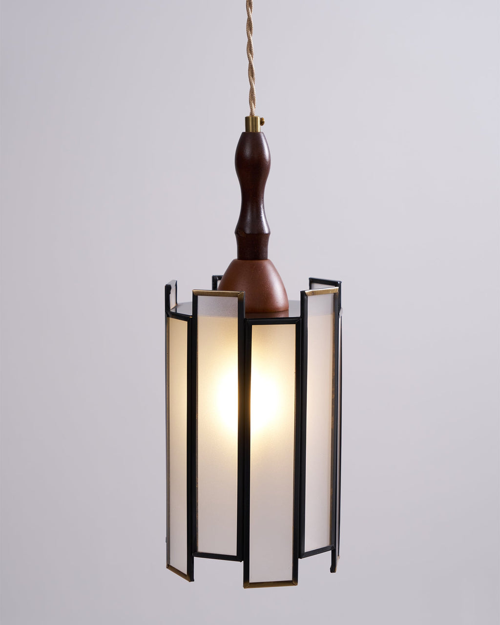 Lit Clérachic frosted-panel pendant against a pale wall, its slim dark frame, brass edges and wooden finial in sharp focus.
