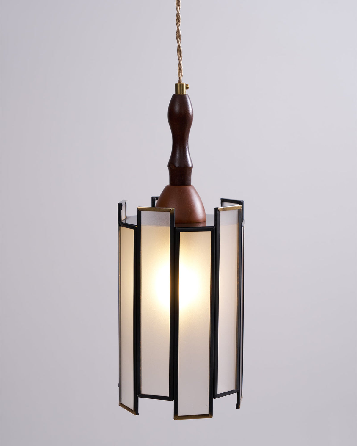 Lit Clérachic frosted-panel pendant against a pale wall, its slim dark frame, brass edges and wooden finial in sharp focus.