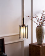 Clérachic frosted-panel pendant hung before a panelled wall, beside a stoneware vase of blossom on a wooden plinth.