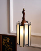 Lit Clérachic frosted-panel pendant beside a framed gold botanical print, against a cream panelled wall.