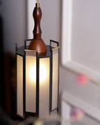 Close view of the lit Clérachic frosted-panel pendant, its dark frame and brass-edged panels against pale wall mouldings.
