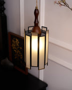 A Clérachic frosted-panel pendant lit above a dark table, with a framed gold botanical picture and blossom beside it.