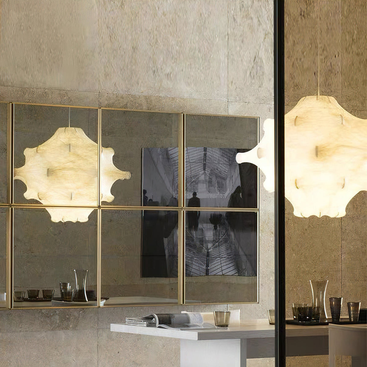 A lit white Clérachic pendant is reflected in a gold-framed mirrored panel, next to a second one at the right edge.