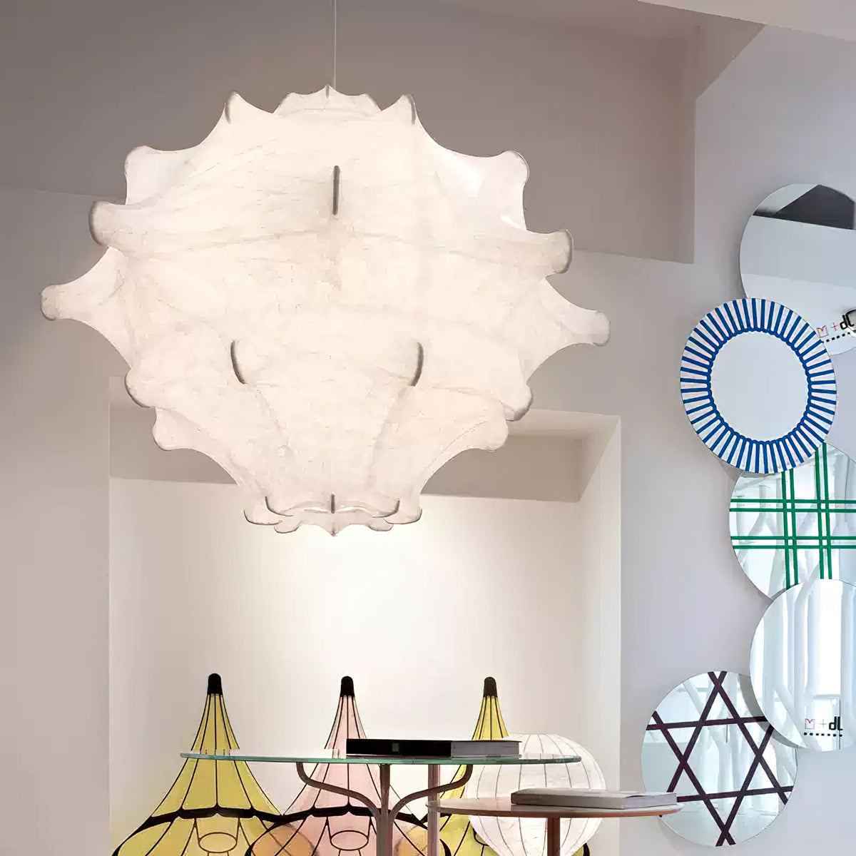 A large white Clérachic pendant hangs in a bright showroom, beside round patterned mirrors and coloured shades.