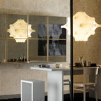 A lit Clérachic pendant in warm tones is reflected in mirrored panels, above a white table and a wooden chair.
