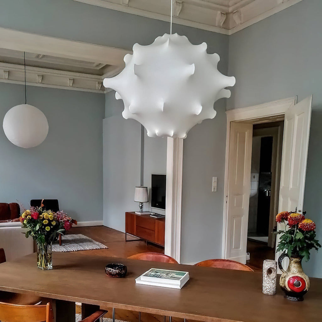 White Clérachic pendant above a long wooden table with flowers and a book, in a room with pale blue walls.