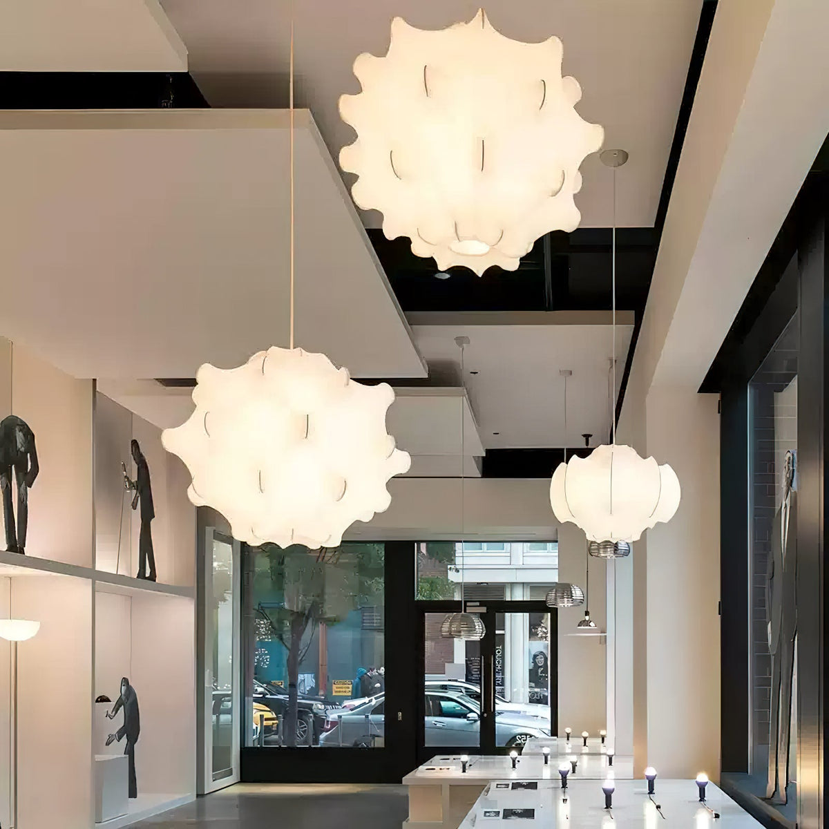 Two white Clérachic pendants and a smaller globe shade glow in a long shop with display niches and a glass front.
