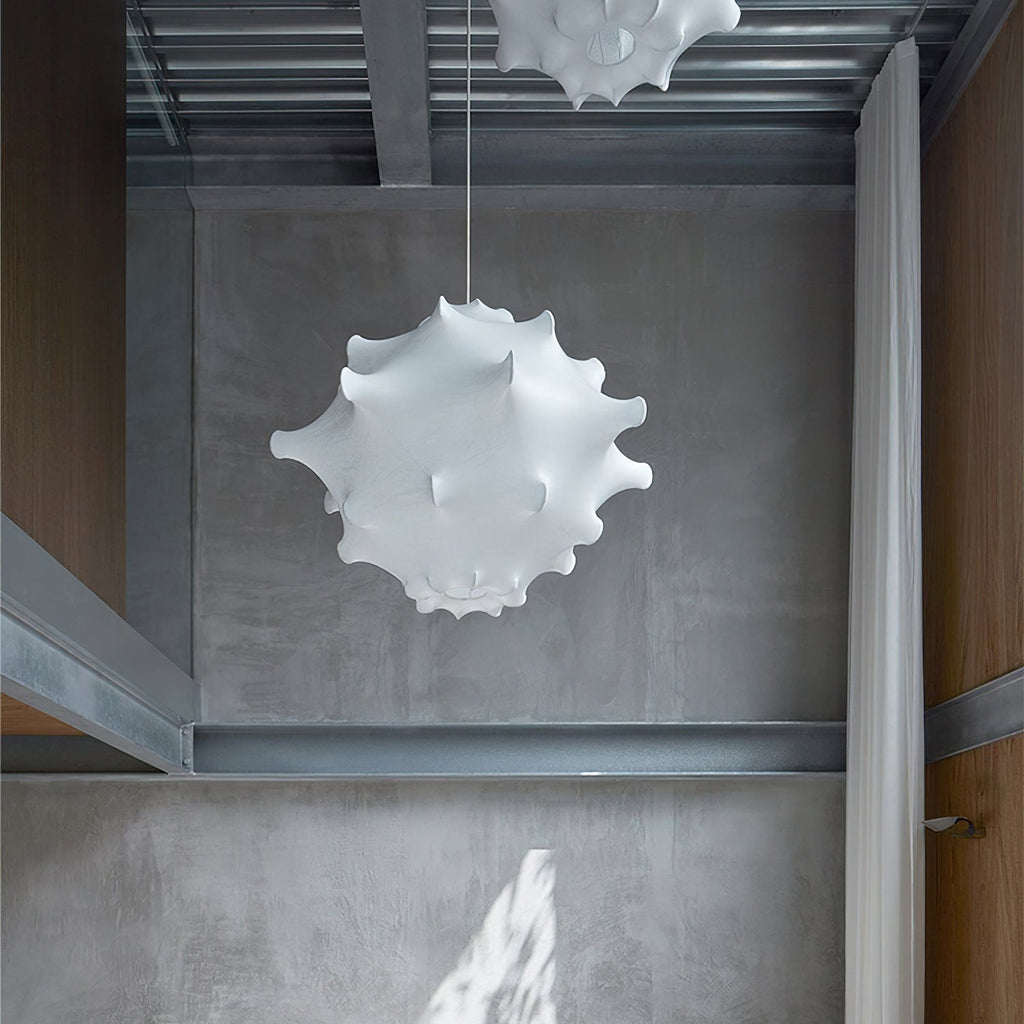 A white Clérachic pendant hangs in a concrete-walled space with steel beams, with a second shade just visible above.