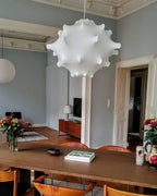 A tighter view of the white Clérachic pendant above a wooden table, with a vase of orange flowers on the right.