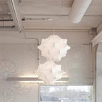 Two white Clérachic pendants hang one above the other in a pale loft with exposed ducting and a lace-patterned wall.