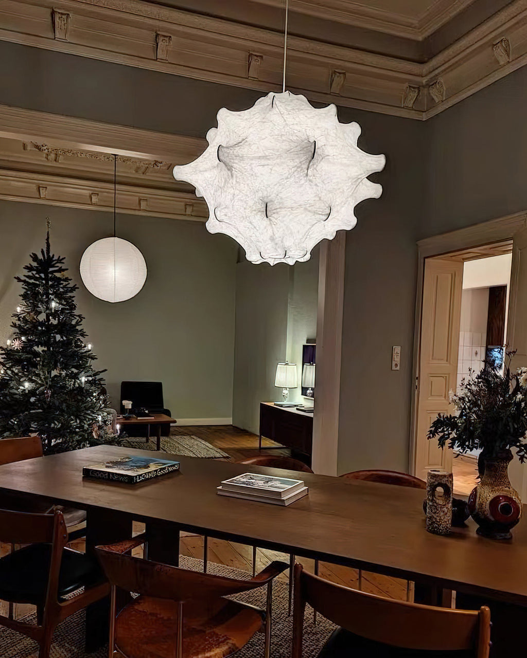 A white Clérachic pendant and a paper globe hang in a room with a Christmas tree and a long wooden table.