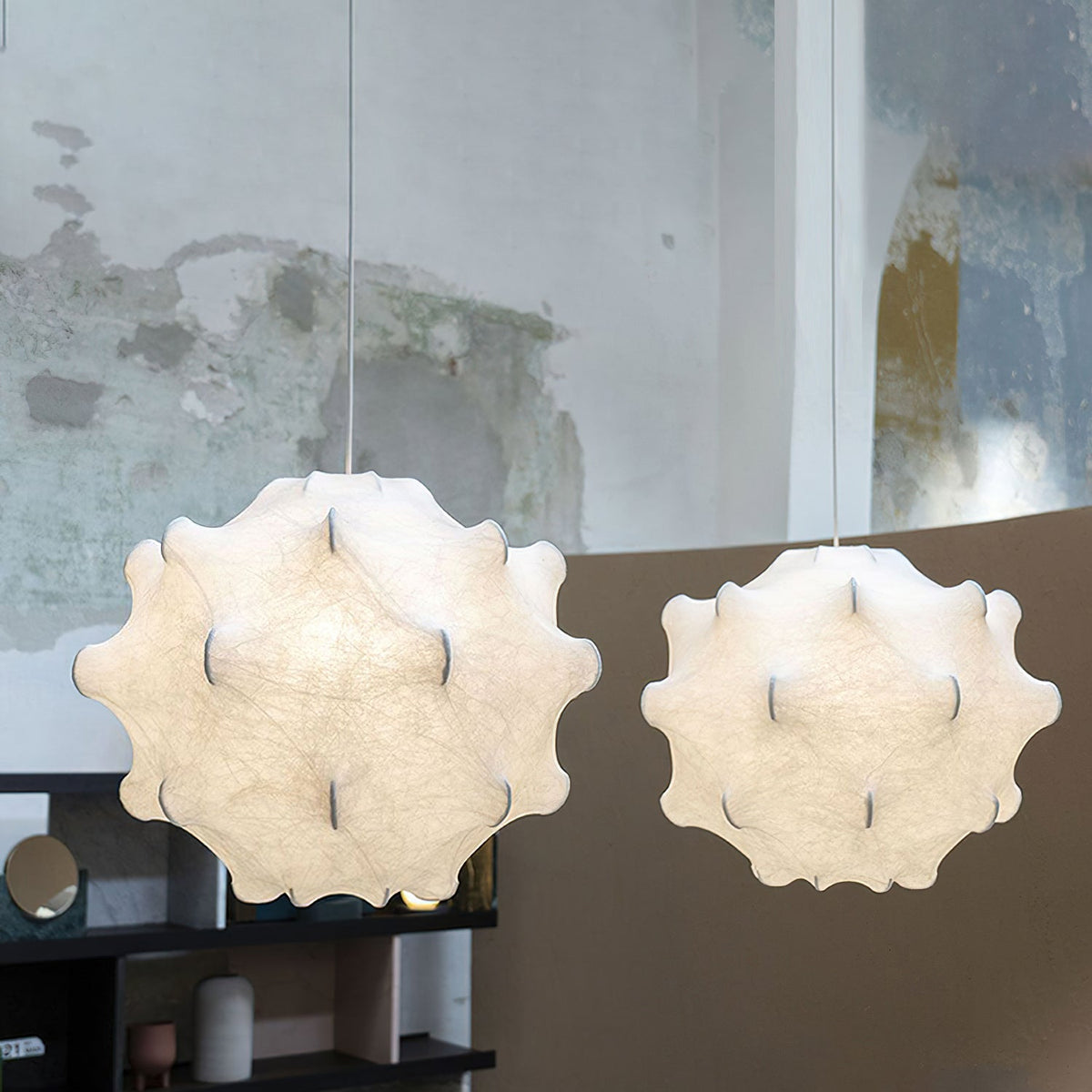 Two white Clérachic pendants glow side by side in front of a curved plaster wall with a shelf below.