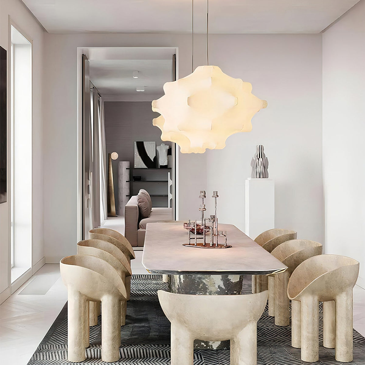 A warm-lit Clérachic pendant hangs above a long pale dining table with cream sculptural chairs.
