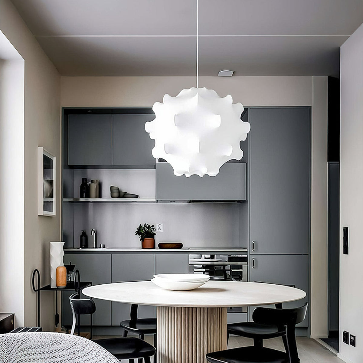 A white Clérachic pendant hangs in a grey kitchen, above a round table with a ribbed base and black chairs.