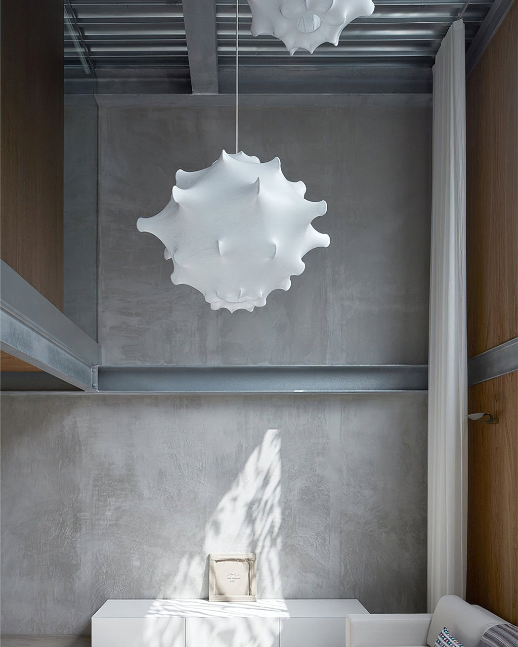 A small white Clérachic pendant hangs in a concrete stairwell with a steel beam, with another shade above.