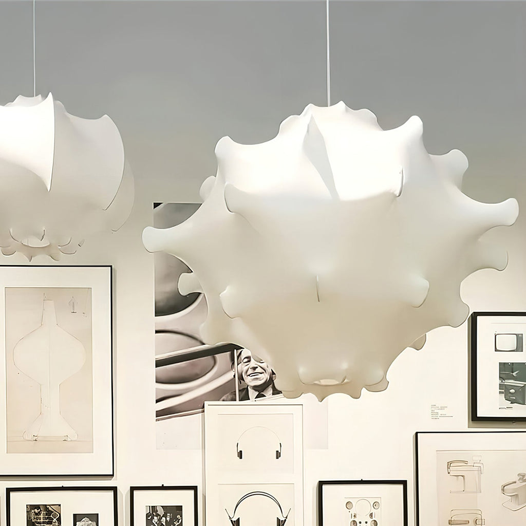 A white Clérachic pendant hangs in front of a wall of black-framed prints and drawings, with a second shade at left.