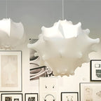 A white Clérachic pendant hangs in front of a wall of black-framed prints and drawings, with a second shade at left.