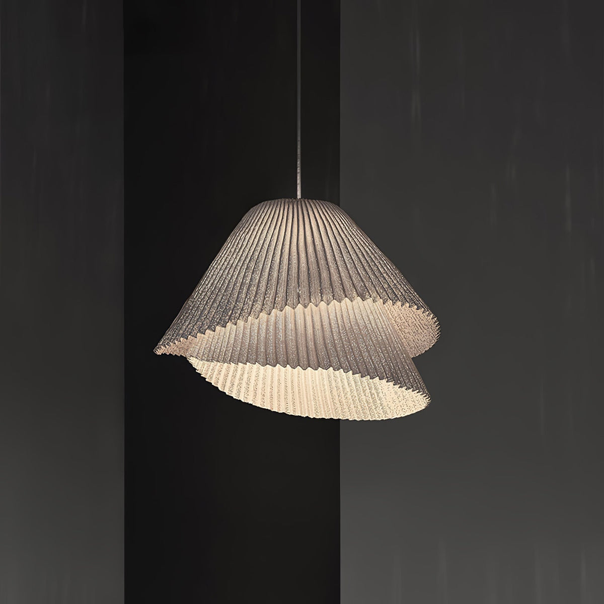 Clérachic pleated pendant lamp photographed against a dark charcoal background, its wave-edged lower layer lit from inside.