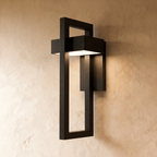 This Clérachic wall light's acrylic strip glows warmly inside its black steel geometric frame on a plaster wall.