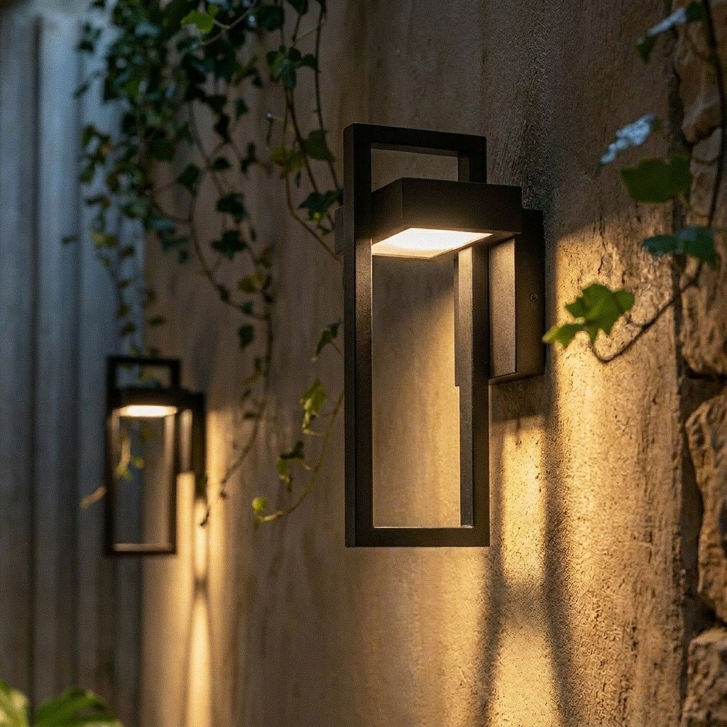At dusk, two Clérachic steel wall lights cast a warm glow beside a glazed door in the same paved courtyard.