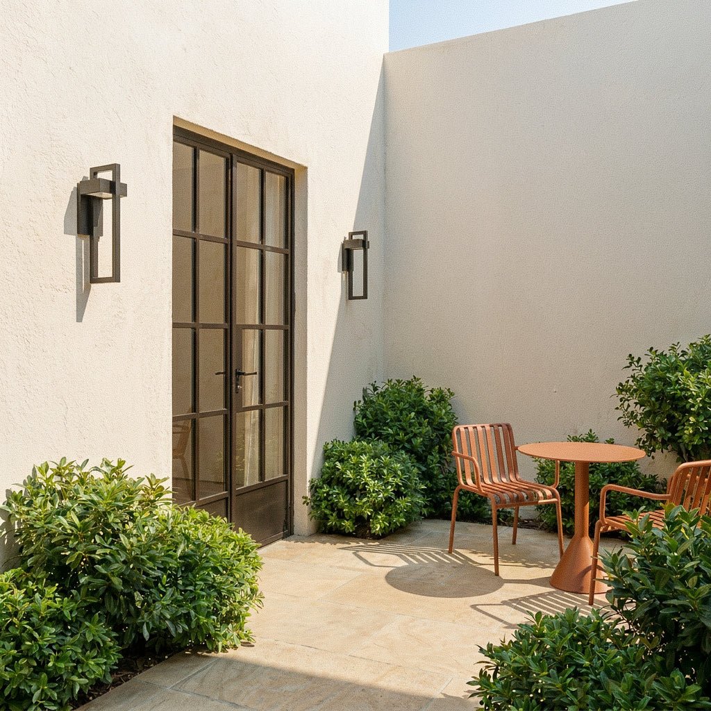 Two Clérachic steel wall lights bracket a paneled front door, boxwood planters and a woven doormat by day.