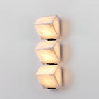 Three stepped alabaster blocks of this Clérachic wall light glow warm on a pale wall, with soft veining visible in the stone.