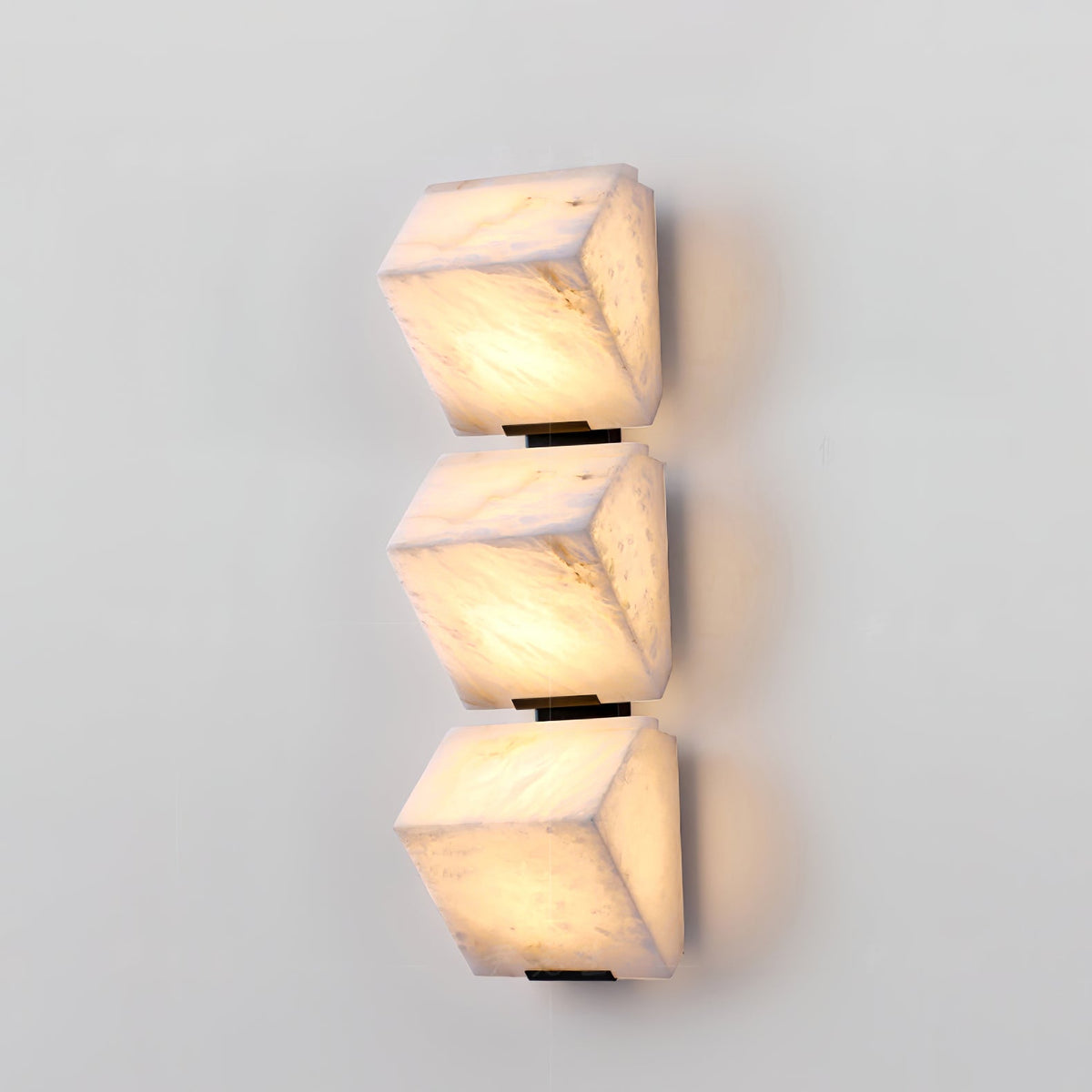 Three stepped alabaster blocks of this Clérachic wall light glow warm on a pale wall, with soft veining visible in the stone.