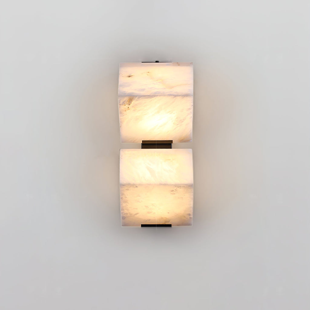 A two-block Clérachic alabaster wall light glows on a pale wall, each block sitting above its own slim black plate.