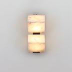 A two-block Clérachic alabaster wall light glows on a pale wall, each block sitting above its own slim black plate.