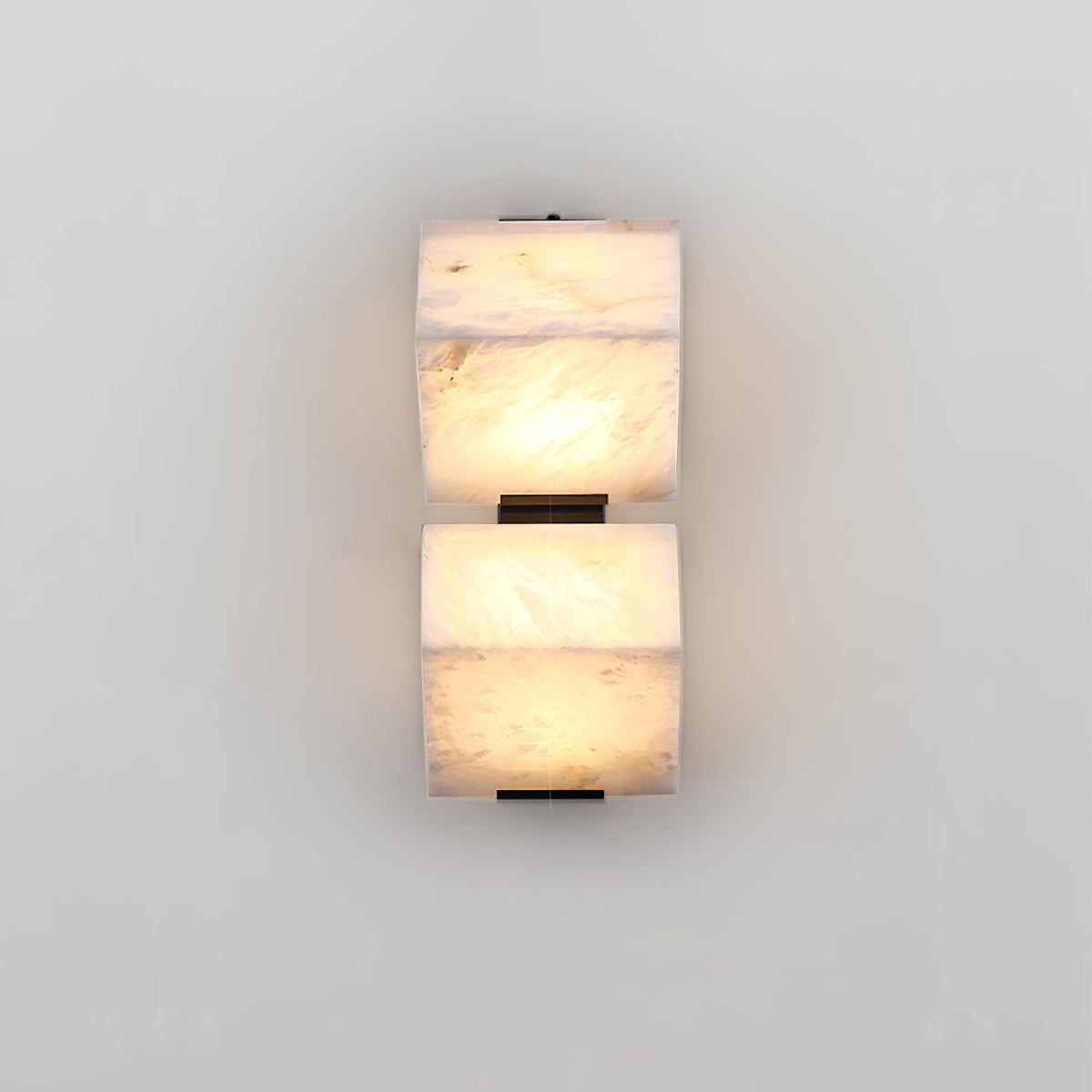 A two-block Clérachic alabaster wall light glows on a pale wall, each block sitting above its own slim black plate.