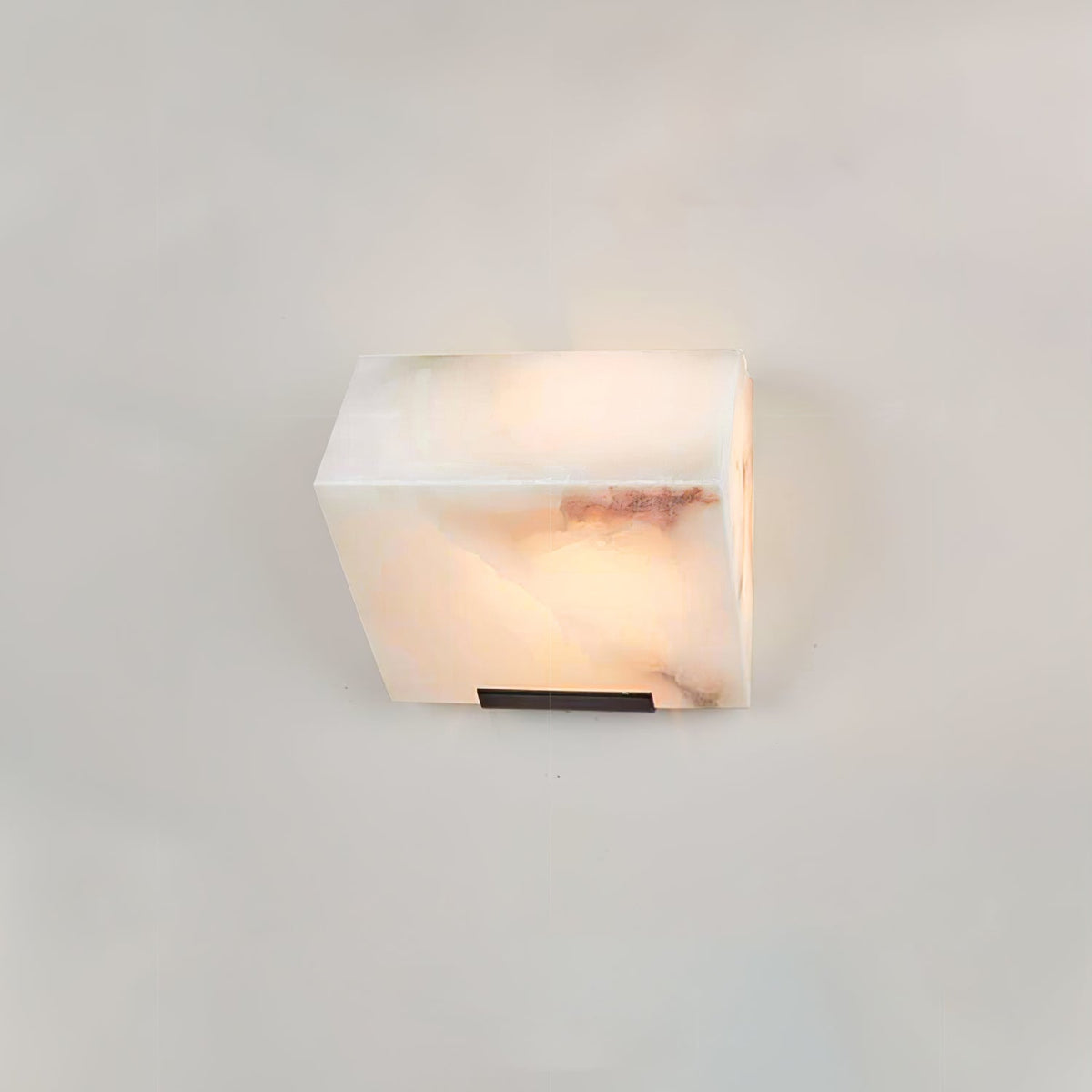 A single Clérachic alabaster block wall light on a pale wall, its rose-brown veining showing through the lit stone.