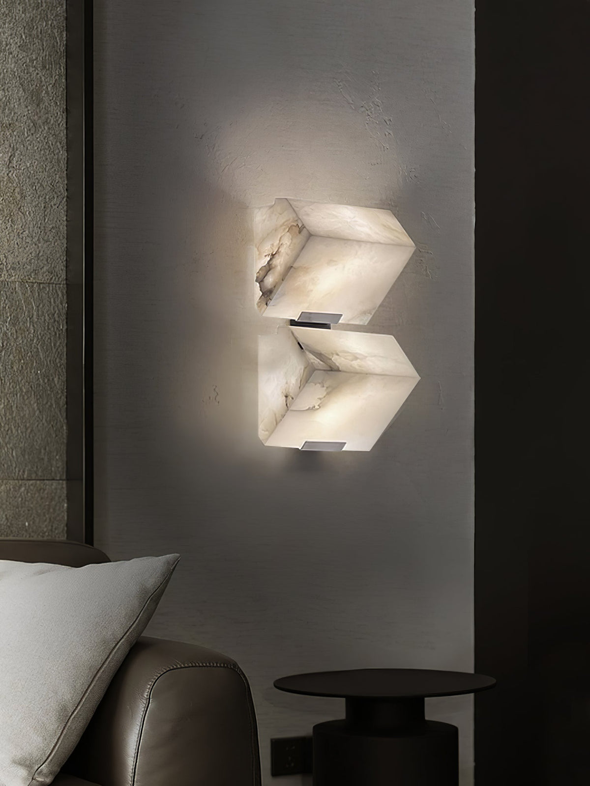 A two-block Clérachic alabaster wall light glows on a dark grey wall above a leather armchair, a pale cushion and a small black side table.