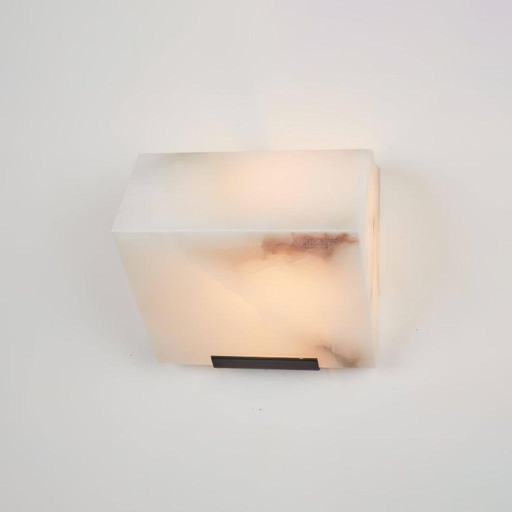 Close view of a single Clérachic alabaster block on a pale wall, showing its brown veining and a slim black wall plate beneath.