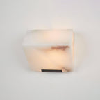 Close view of a single Clérachic alabaster block on a pale wall, showing its brown veining and a slim black wall plate beneath.
