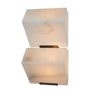 Close cut-out view of a two-block Clérachic alabaster wall light, the upper block showing brown veining above the lit lower block.