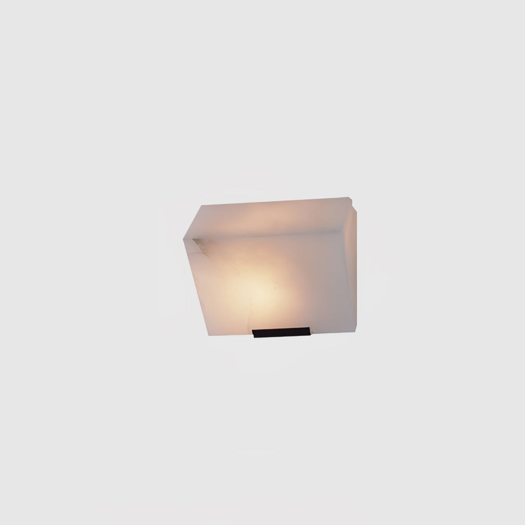 A single Clérachic alabaster block wall light on a light grey backdrop, glowing warm above a slim black wall plate.