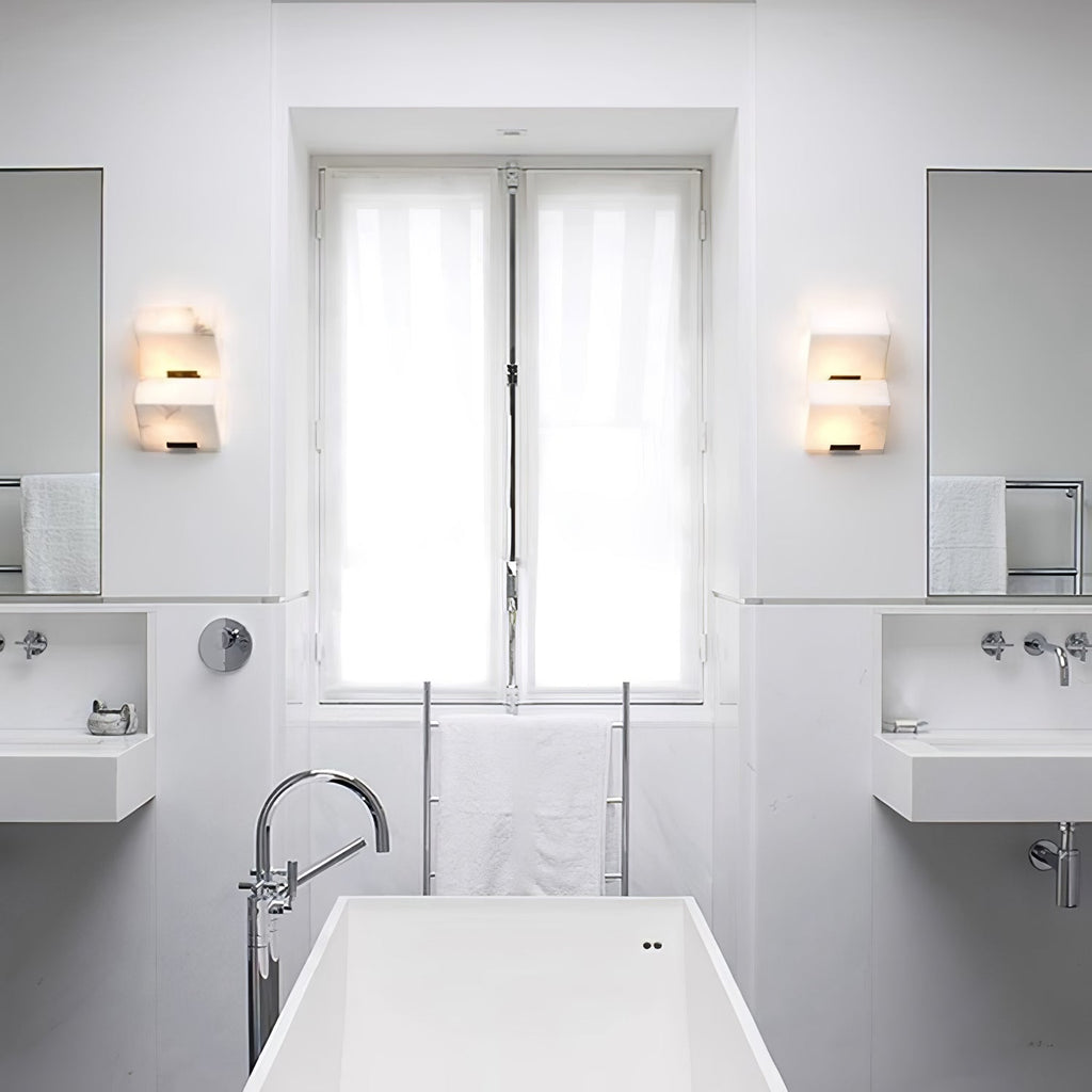 A bathroom with two Clérachic alabaster wall lights either side of the window, above a white freestanding bath and wall-mounted basins.