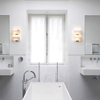A bathroom with two Clérachic alabaster wall lights either side of the window, above a white freestanding bath and wall-mounted basins.