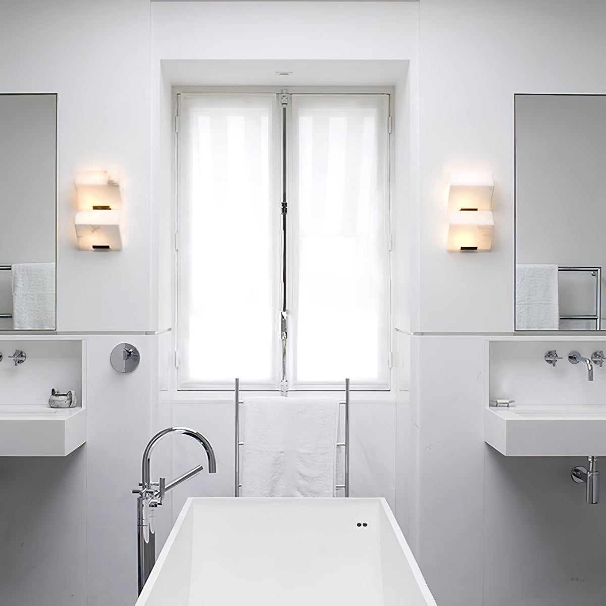A bathroom with two Clérachic alabaster wall lights either side of the window, above a white freestanding bath and wall-mounted basins.