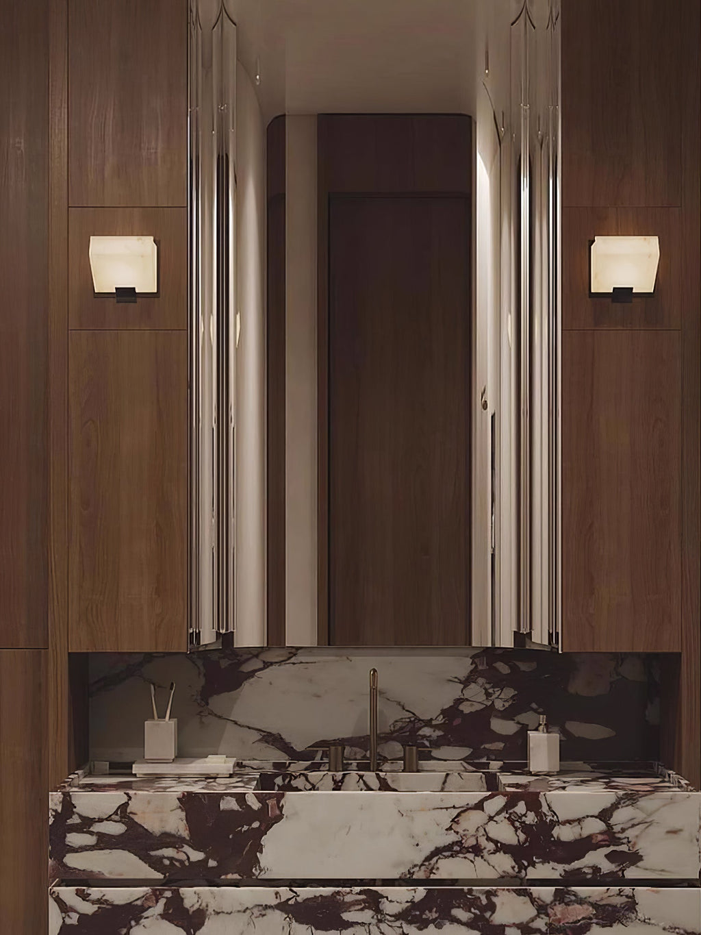 A Clérachic alabaster wall light on each side of a tall mirror above a dark marble vanity in a walnut-panelled bathroom.