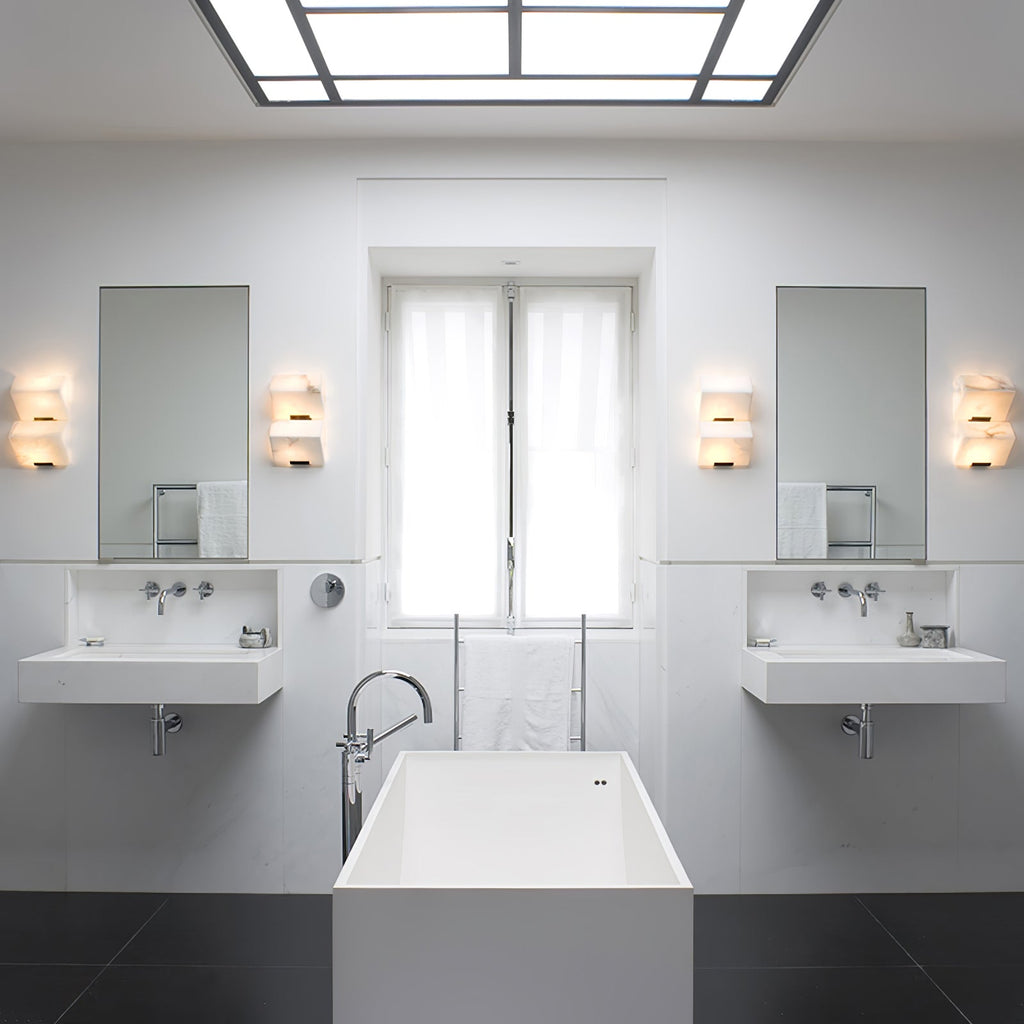 Four Clérachic alabaster wall lights in pairs beside two mirrors in a white bathroom with twin basins and a freestanding bath.