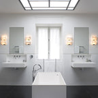 Four Clérachic alabaster wall lights in pairs beside two mirrors in a white bathroom with twin basins and a freestanding bath.