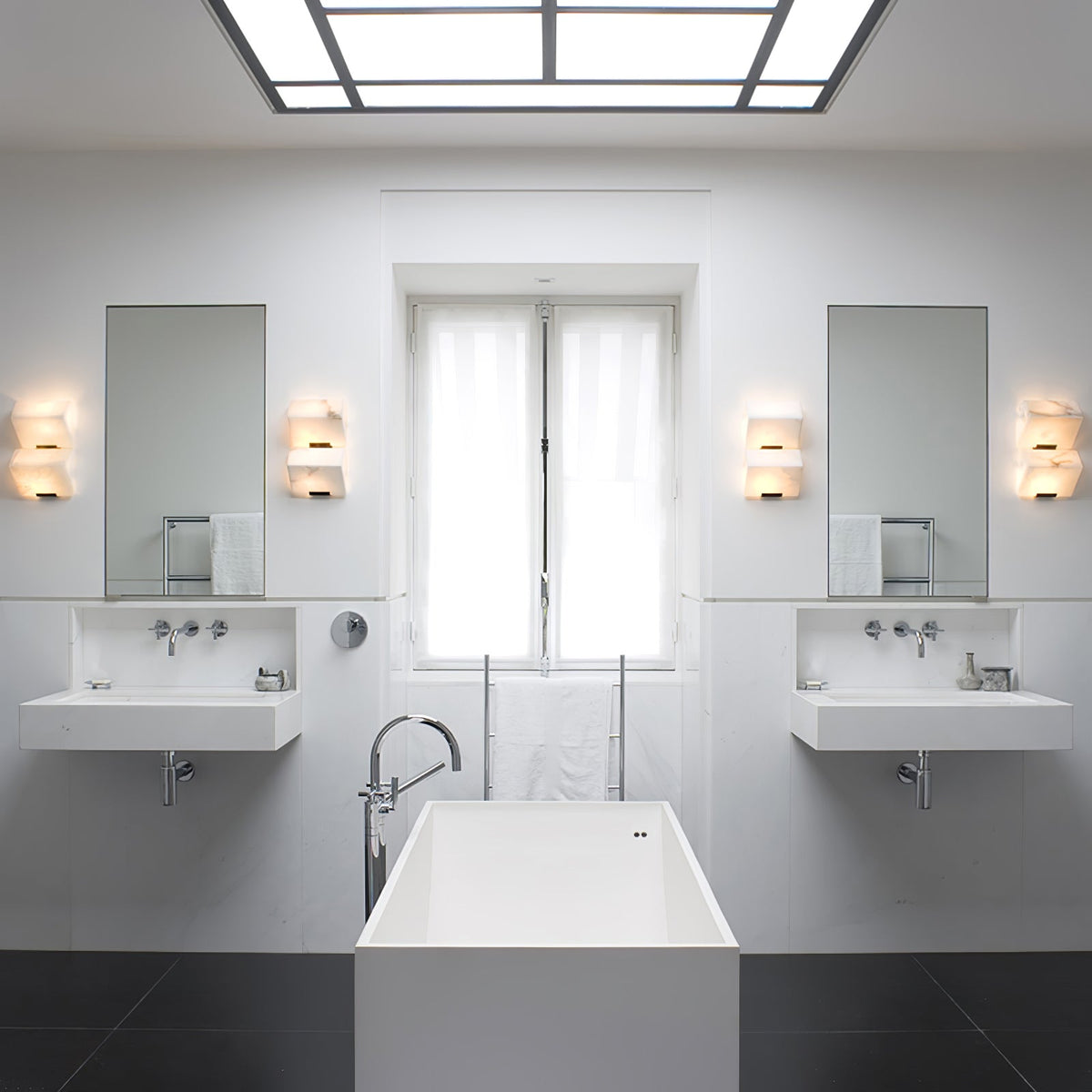 Four Clérachic alabaster wall lights in pairs beside two mirrors in a white bathroom with twin basins and a freestanding bath.