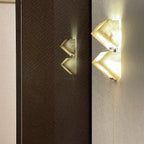 Two Clérachic alabaster wall lights glow on a dark woven wall panel and a pale wall, the brighter one showing the stepped blocks clearly.