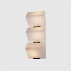 A three-block Clérachic alabaster wall light on a light grey backdrop, its blocks lit softly from within.