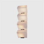 A four-block Clérachic alabaster wall light on a light grey backdrop, the stepped blocks lit softly above black plates.