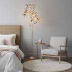 Clérachic agate floor lamp lit beside a bed and a pale armchair, with a small gold side table and a round white rug.