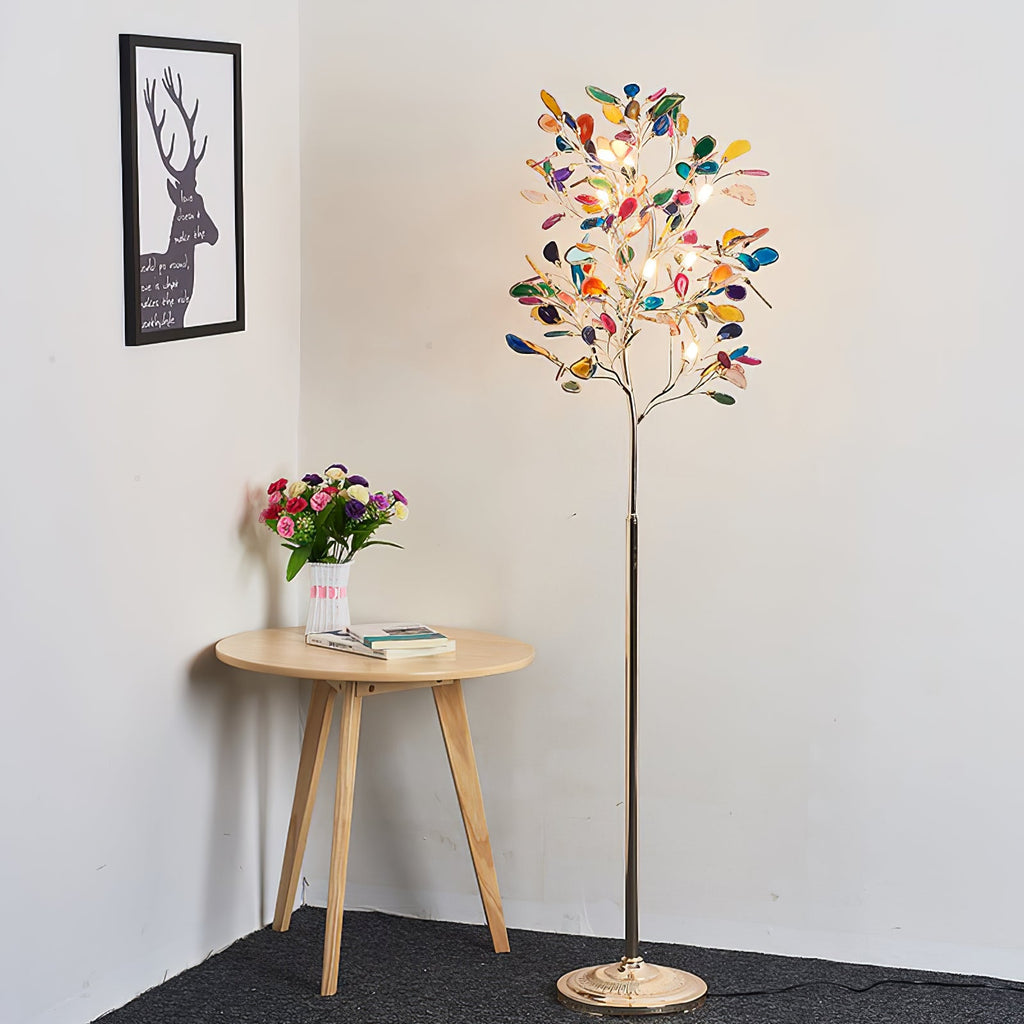 Lit Clérachic agate floor lamp in a white corner, with a round wooden side table, a vase of flowers and a framed stag print.