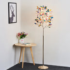 Lit Clérachic agate floor lamp in a white corner, with a round wooden side table, a vase of flowers and a framed stag print.