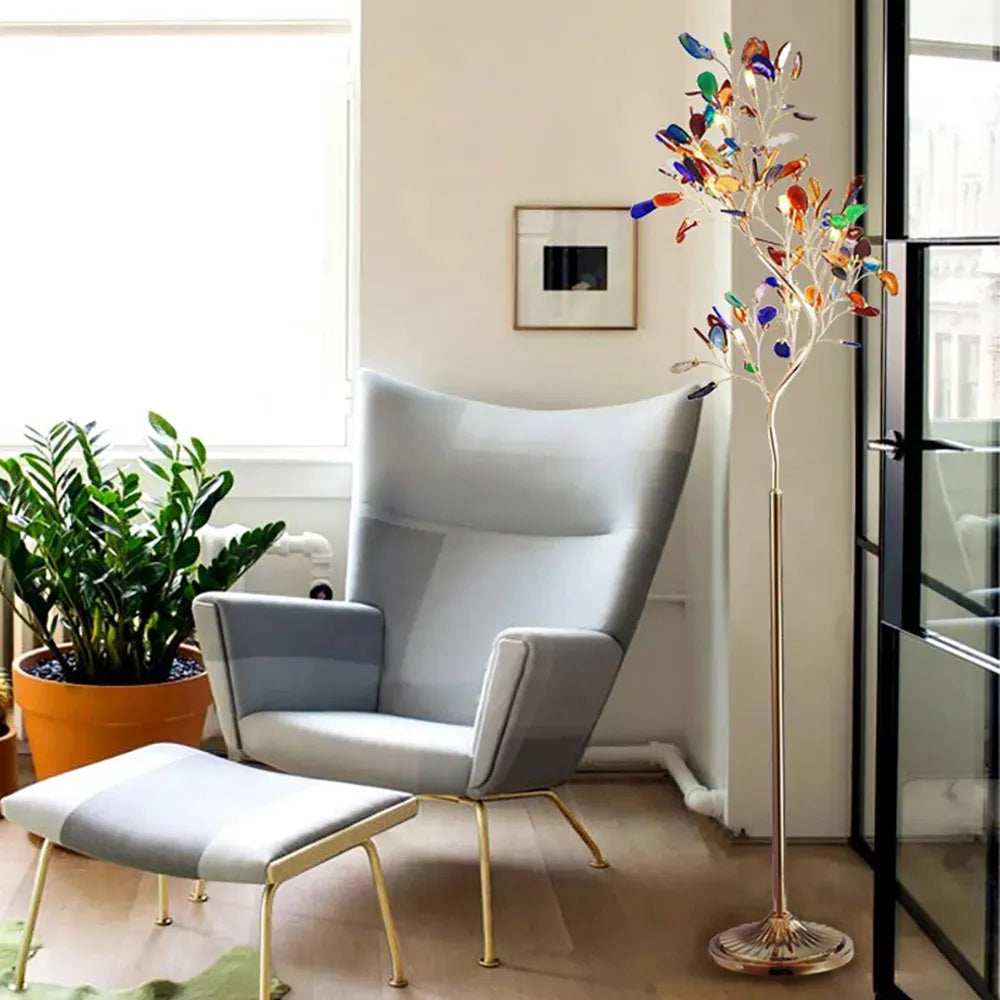 Clérachic agate floor lamp beside a pale grey wingback chair and footstool, with a large plant by a glazed door.